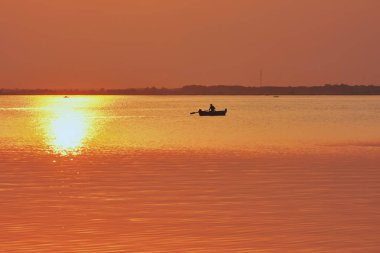 Gölde gün batımı. Güneşli sularda balıkçıyla tekne gezisi..