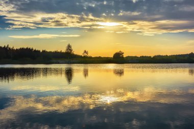 Gölde gün batımı - güneş kıyı şeridinin siluetinin üzerinde.