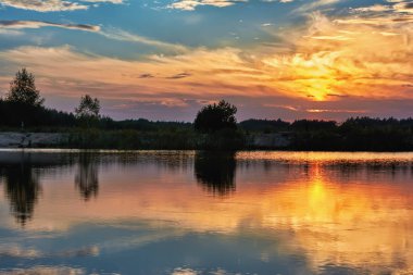 Gölde gün batımı - kıyı şeridinin silueti üzerindeki bulutlarla gökyüzü.