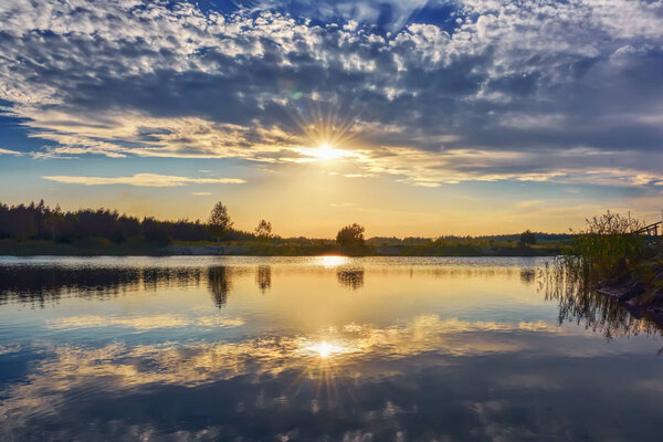Sunset on the lake - sky with clouds, sun over silhouette of coastline.