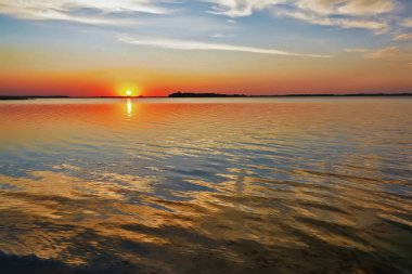Gölün üzerinde güneş ve bulutlarla gün batımı.