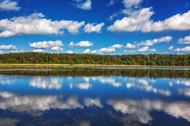 Gölde güneşli bir gün. Orman ve bulutlar suya yansıyor..