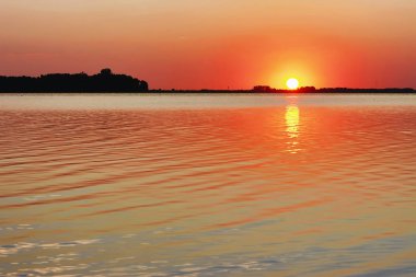 Gölün üzerinde gün batımı - güneş kıyı şeridinin siluetinin üzerinde.