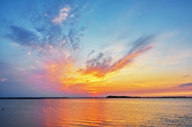 Gölün üzerinde gün batımı - bulutlar siluet kıyı şeridinde yansıyor suya.