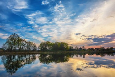 Gölün üzerinde alacakaranlık - ağaçlar ve binalarla kıyı şeridi.