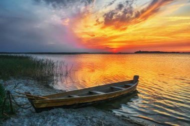 Gölün üzerinde gün batımı - kumlu sahilde ahşap tekne.