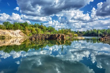 Ormanlı Rocky Shore Gölü. Mavi gökyüzü suya yansıyan bulutlarla.