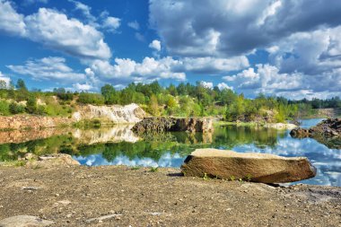 Ormanlı Rocky Shore Gölü. Mavi gökyüzü ve suya yansıyan bulutlar..