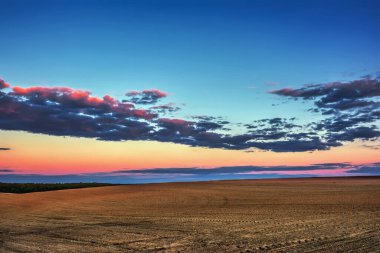 Akşam kırsal manzarası - mavi gökyüzü ve gün batımında saban tarlaları üzerinde bulutlar.
