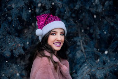 Dışarıda Noel Baba şapkası takan gülümseyen genç bir kadın.