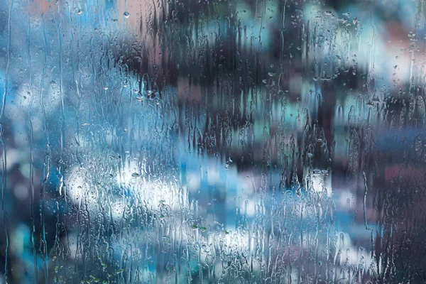 Textured wet window glass with rain drops and abstract light blue blurs