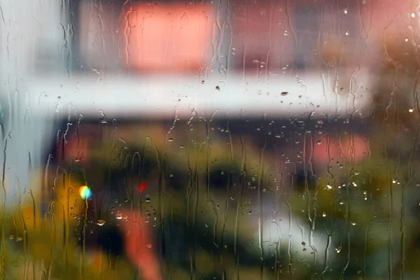 Wet window glass with rain drops and colorful abstract blurs and silhouettes on the street