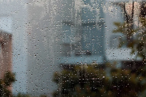 雨滴と灰色 茶色と黄色の抽象的な青と通りのシルエットがたくさんある湿った窓ガラス — ストック写真