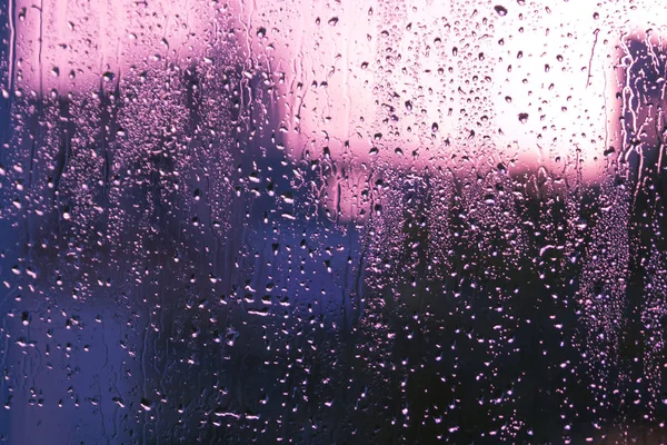 Wet window glass with lots of rain drops and abstract gray, blue and pink blurs