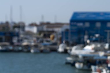 Bulanık bir arka plan, mavi deniz ve limanda demirlemiş tekneler.