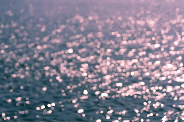 Blurred background with lots of pink sparkles on aquamarine sea water surface