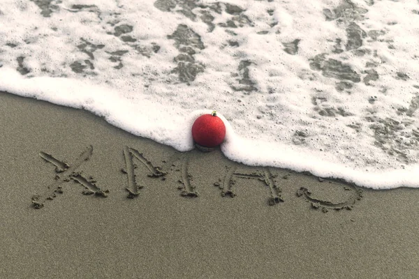 Wortweihnacht Auf Dem Nassen Sand Strand Eine Rote Weihnachtskugel Und — Stockfoto