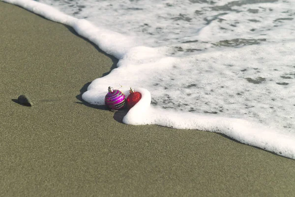 Dvě Barevné Vánoční Koule Písečné Pláži Pěnivé Mořské Vlně — Stock fotografie