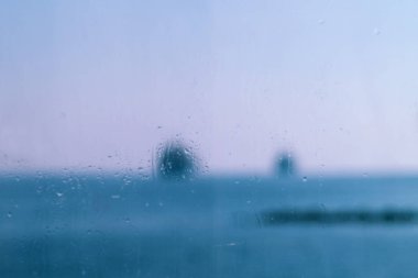 Wet window glass with water drops and a blurred view of the blue sea and pinkish sky
