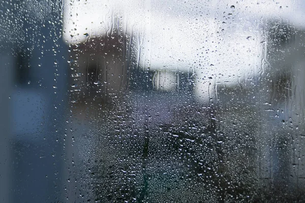 Nasses Fensterglas Mit Wassertropfen Und Verschwommenen Häuserformen Vor Dem Blassen — Stockfoto