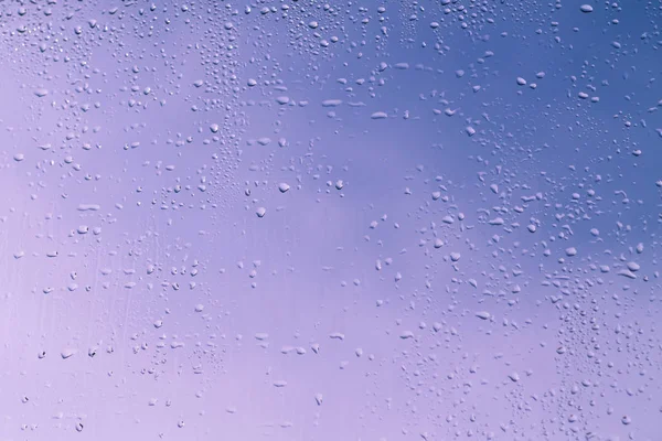 Blue and pink wet window glass with water drops