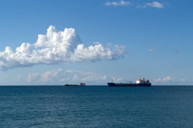 Mavi deniz manzarası, beyaz bulutlu gökyüzü ve ufukta iki gemi. 
