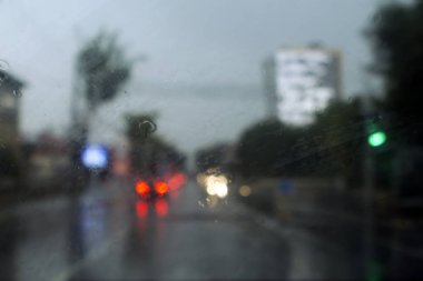 Yağmurda ıslak bir arabanın ön camından geçen renkli ışıkların olduğu bulanık bir yol.