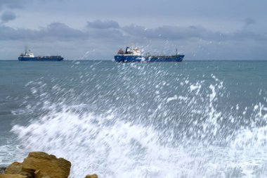 Kara bulutlu gökyüzü, fırtınalı deniz ufukta iki gemi ve bulanık bir dalga.