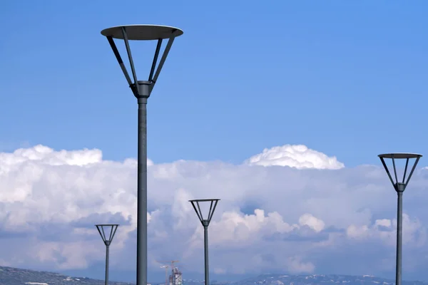 Gray metal street lamps in front of the bright blue sky,  gray clouds and mountains