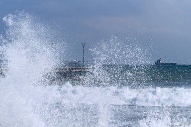 Sea view with a pier and a ship on the horizon through white wave spray