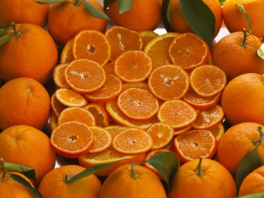 Kabuğu soyulmamış portakal ve mandalina dilimleri. Biraz da yeşil yapraklı portakallarla çevrili.