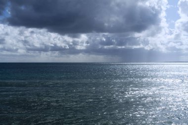 Güneş ışığında parlayan deniz ve yukarıdaki karanlık dramatik gökyüzü.