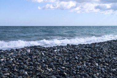 Gri çakıl taşları, deniz ve soluk gökyüzü olan boş bir kiremit plajı. 