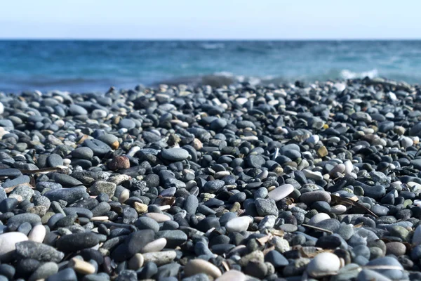 Güneş ışığında kumsalda gri çakıl taşları mavi deniz ve arka planda soluk gökyüzü