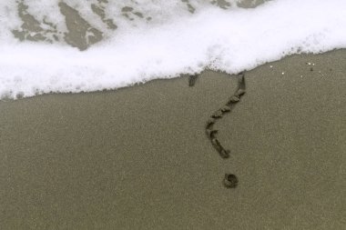 Soru işareti ıslak kumsalda beyaz köpüklü bir deniz dalgası ile yazılmış.