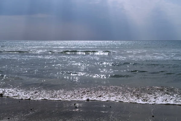 Işıldayan dalgalı deniz ve karanlık bulutlu güneş ışınlarıyla gökyüzü