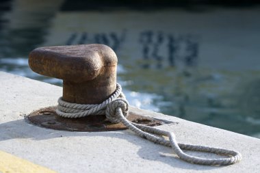 Limandaki bulanık denizin önünde düğümlenmiş bir iple paslı bir demirleme direğine yakın çekim. 