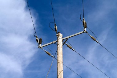 Mavi gökyüzü ve beyaz bulutların önünde güneş ışığıyla kablolu elektrik direği