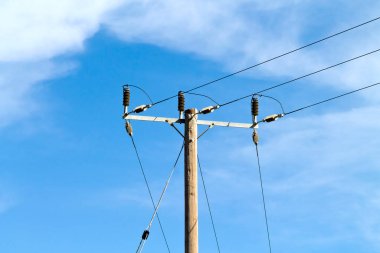 Ahşap elektrik direği, mavi gökyüzünün önünde kablolar, güneş ışığında beyaz bulutlar. 