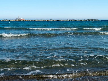 Dalgalı mavi deniz, beyaz köpüklü, taş ahşap ve ufukta gemiler.