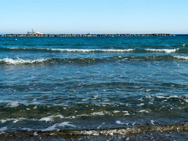 Dalgalı mavi deniz, beyaz köpüklü, taş ahşap ve ufukta gemiler.