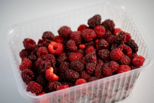 Viele frische Himbeeren in Plastikverpackung auf weißem Rücken — Stockfoto