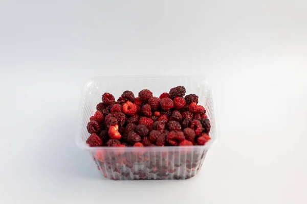 A lot of fresh raspberries in plastic packaging on a white backg — Stock Photo, Image