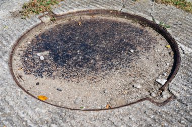 Sokakta demir kapaklı bir rögar kapağı var.