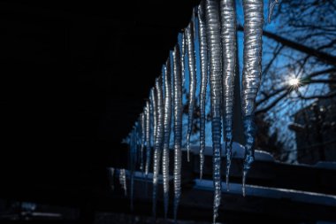 Güneşli havada çatıdan sarkan buz saçakları.