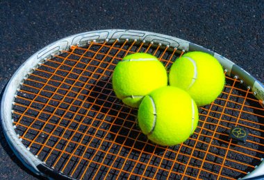 Tenis topları tenis raketinin üzerinde yatıyor.