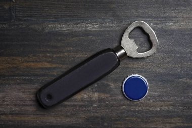 Bottle opener beside a bottle cap lying on a wooden table. High angle view with copy space.