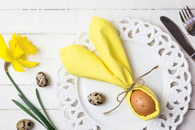 Paskalya Tavşanı gibi peçetede yumurta ve beyaz ahşap masada bahar çiçekleri olan güzel Paskalya sofrası. Kopyalama alanı olan üst görünüm.