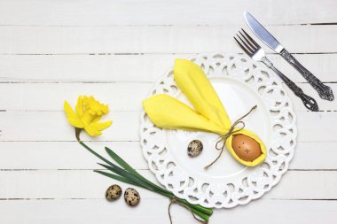 Paskalya Tavşanı gibi peçetede yumurta ve beyaz ahşap masada bahar çiçekleri olan güzel Paskalya sofrası. Kopyalama alanı olan üst görünüm.