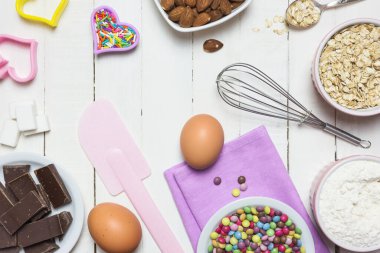 Kek pişirmek için malzemeler ve aletler. Yumurta, un, süt, şeker, fındık, çikolata ve şeker beyaz ahşap masada. Pişirme veya pişirme konsepti.